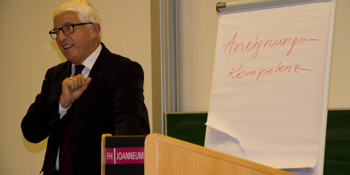 Man im Vordergrund mit Flipchart mit dem Begriff Aneignungskompetenz im Hintergrund.