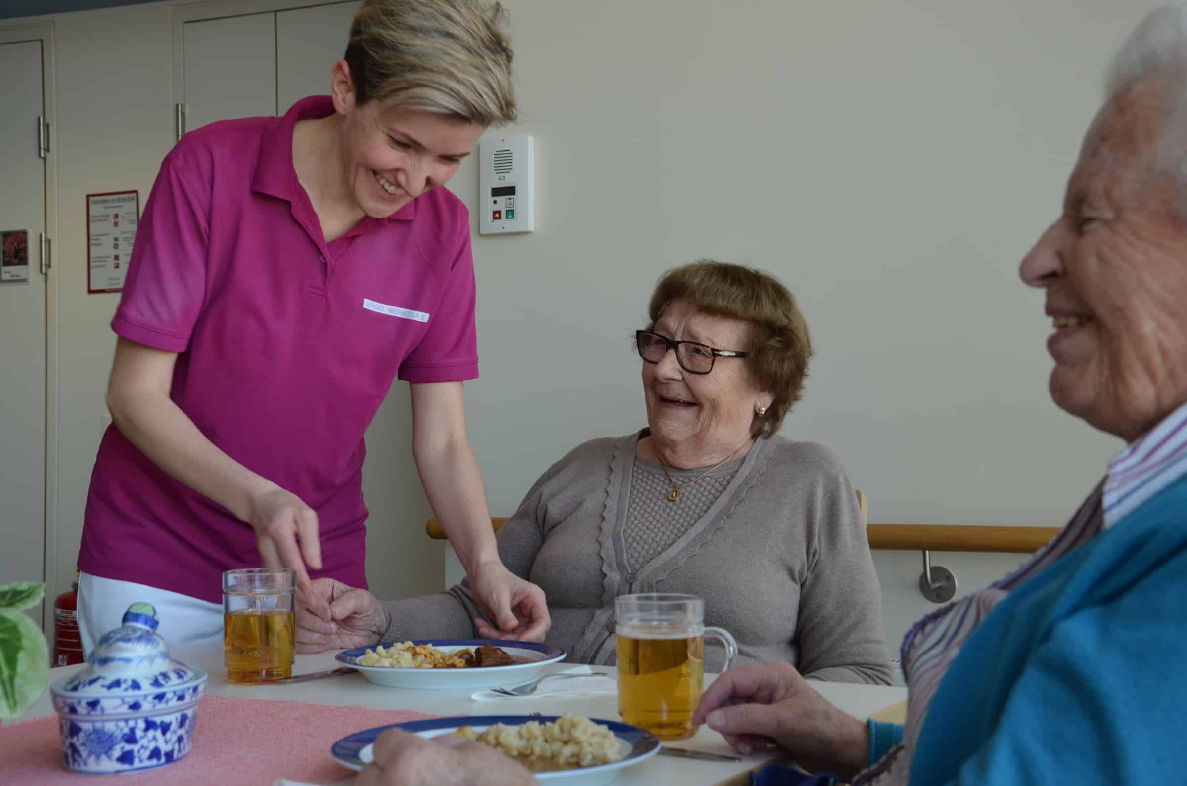 Pflegefrau serviert einer älteren Dame das Essen.