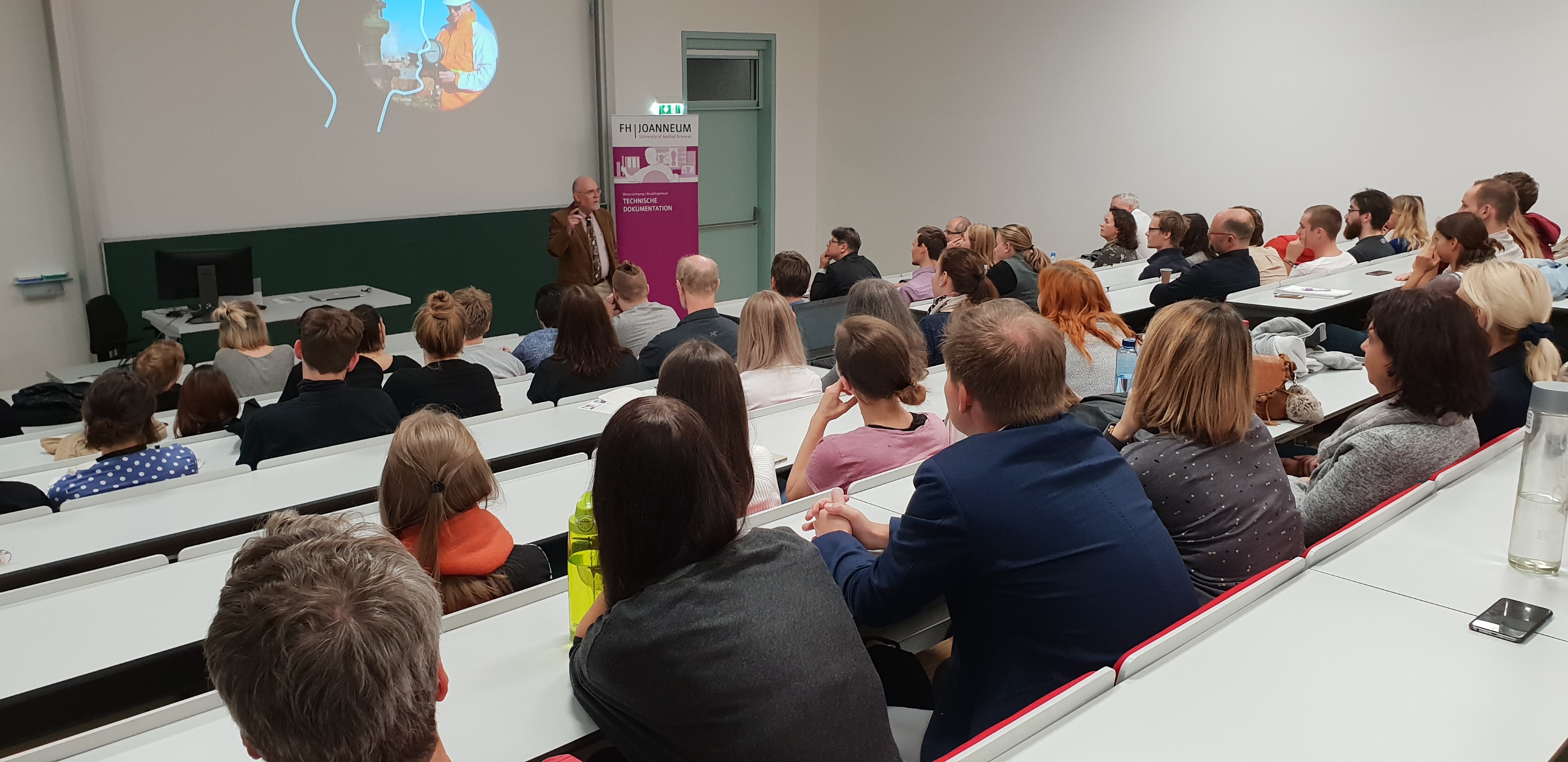 Person bei Vortrag mit Präsentation im Hintergrund.