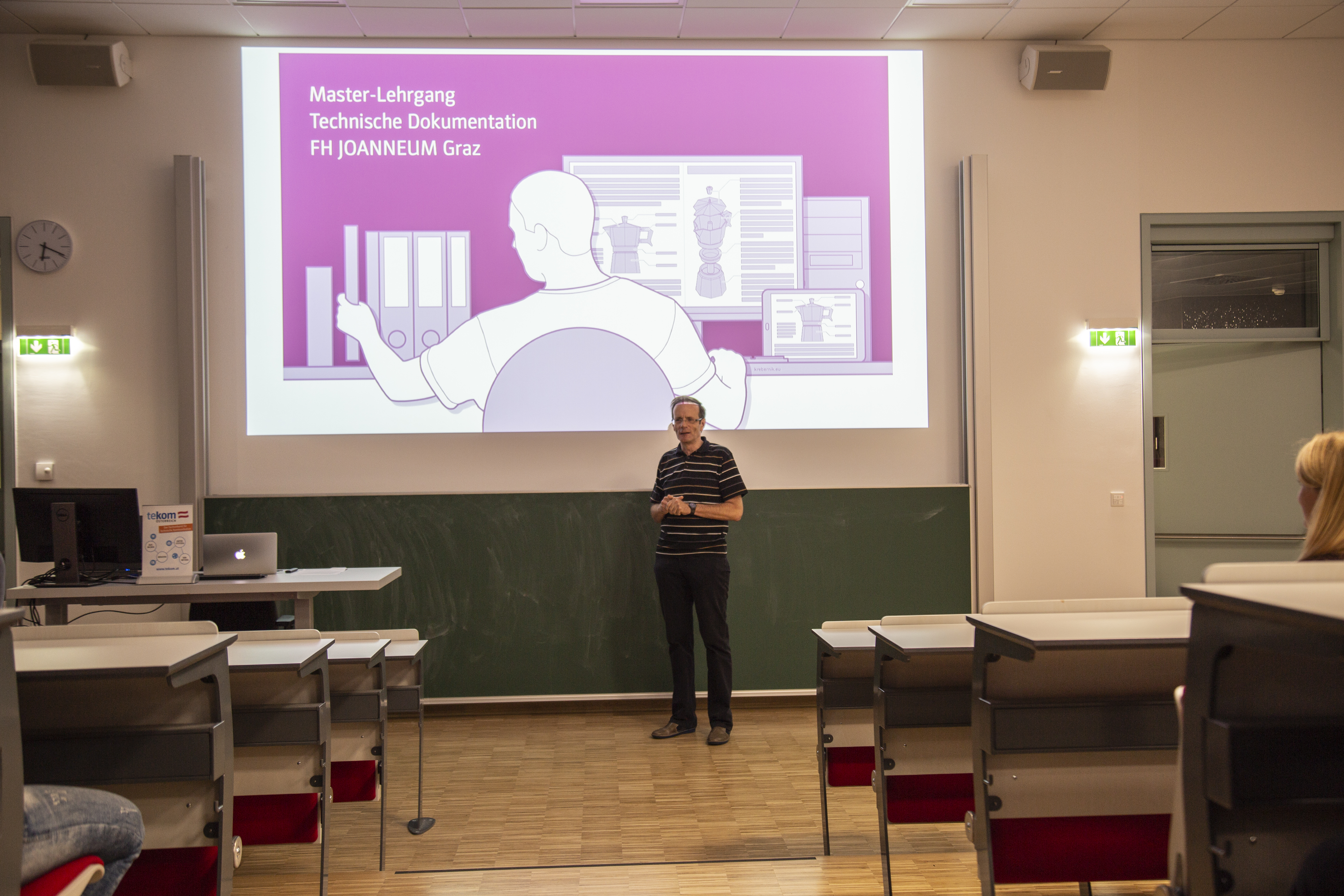 Person bei Vortrag mit Präsentation im Hintergrund.