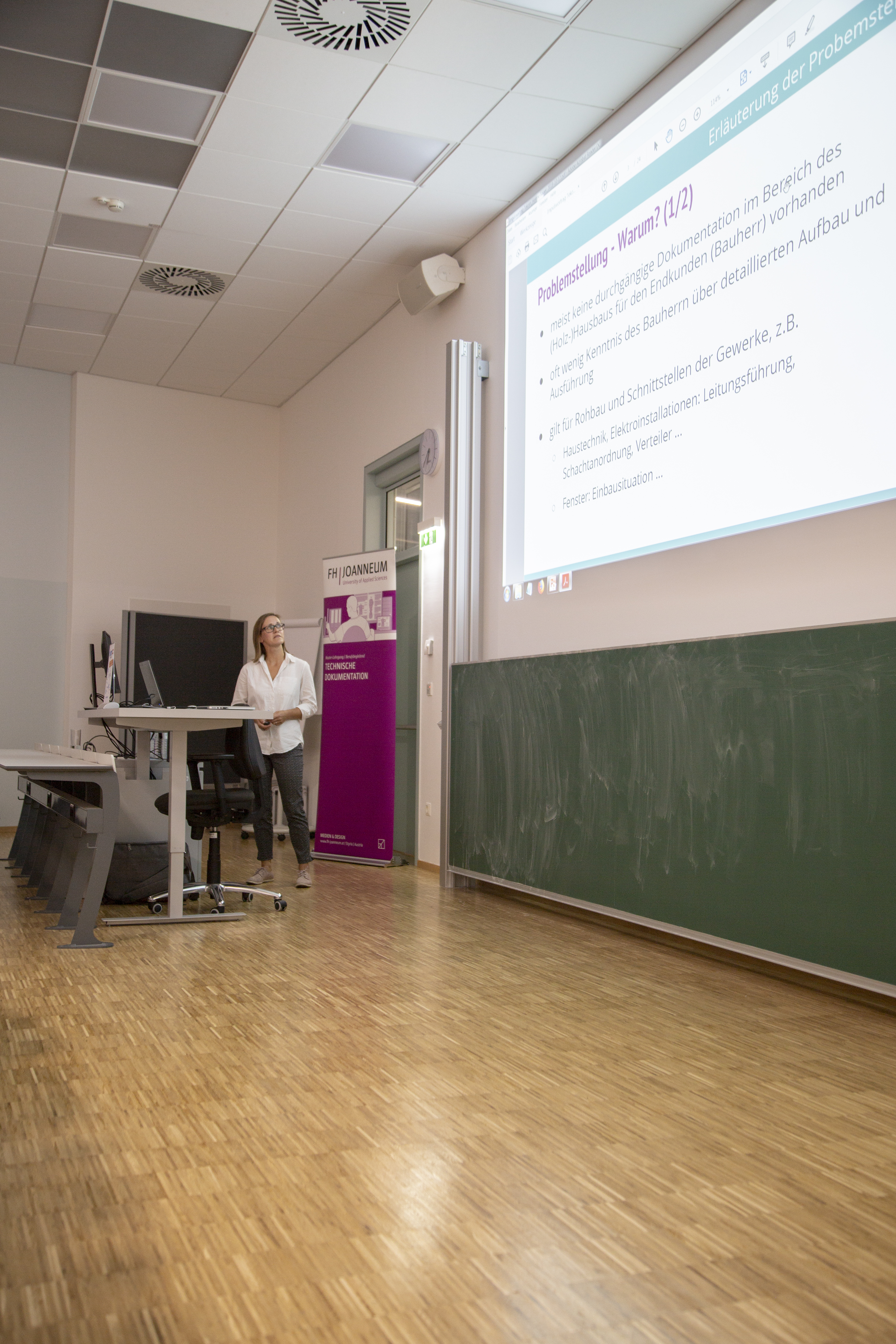 Person bei Vortrag mit Präsentation im Hintergrund.