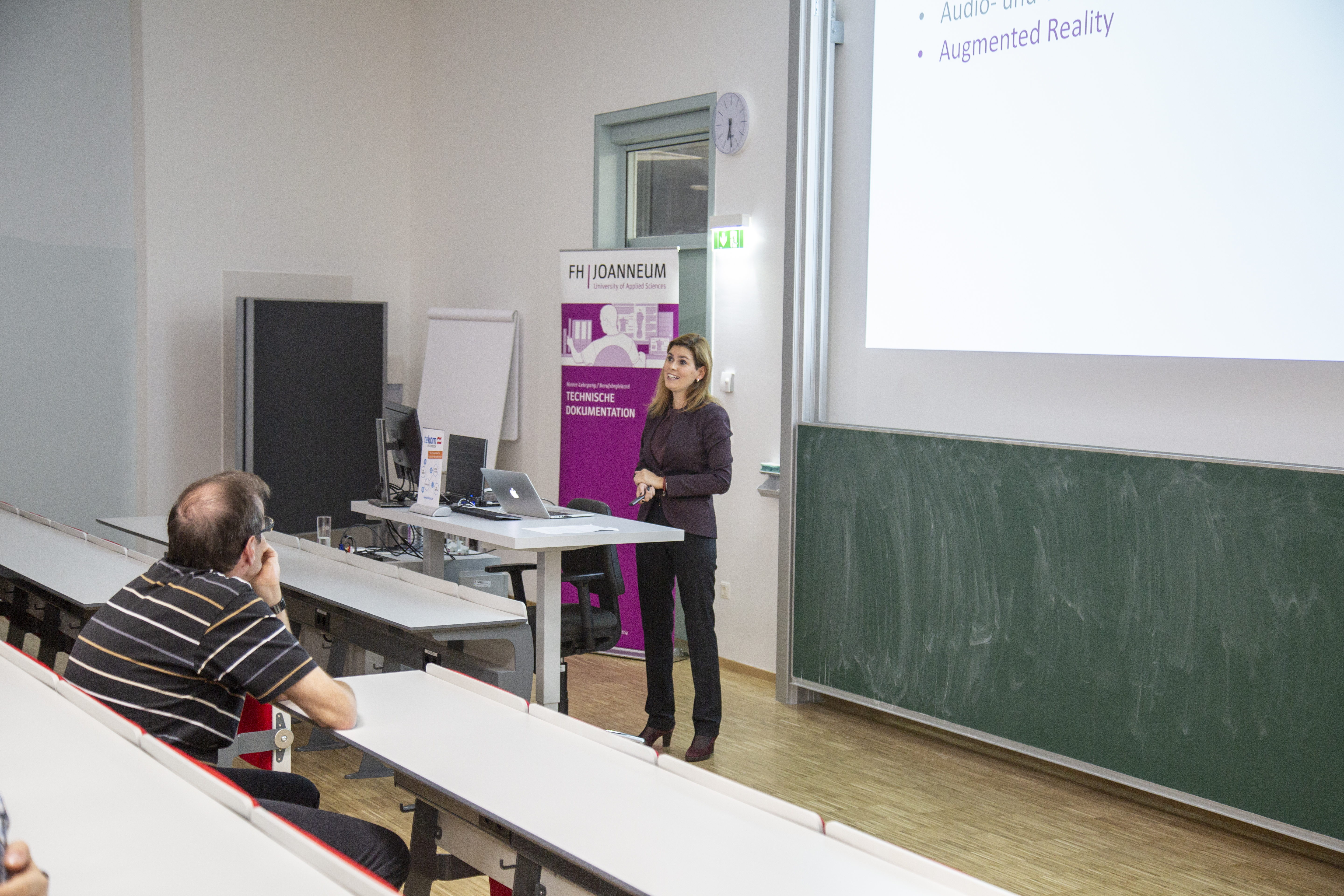 Person bei Vortrag mit Präsentation im Hintergrund.