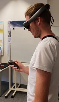 Mann trägt eine Augmented-Reality-Brille und hält einen Controller in der Hand.
