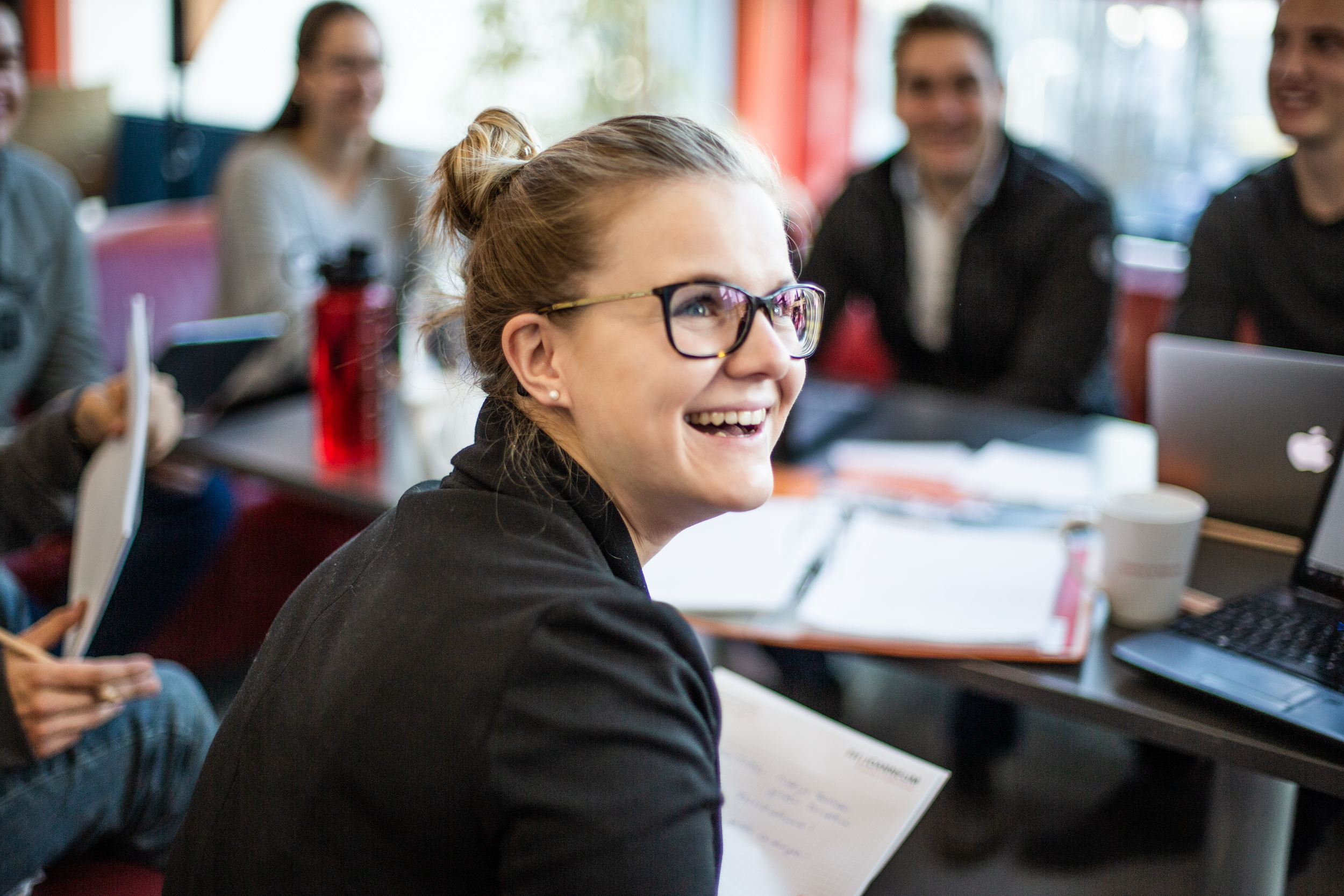 Studierende sitzt mit Kolleginnen und Kollegen an einem Tisch und zeigt sich erfreut über die gelernten Inhalte.