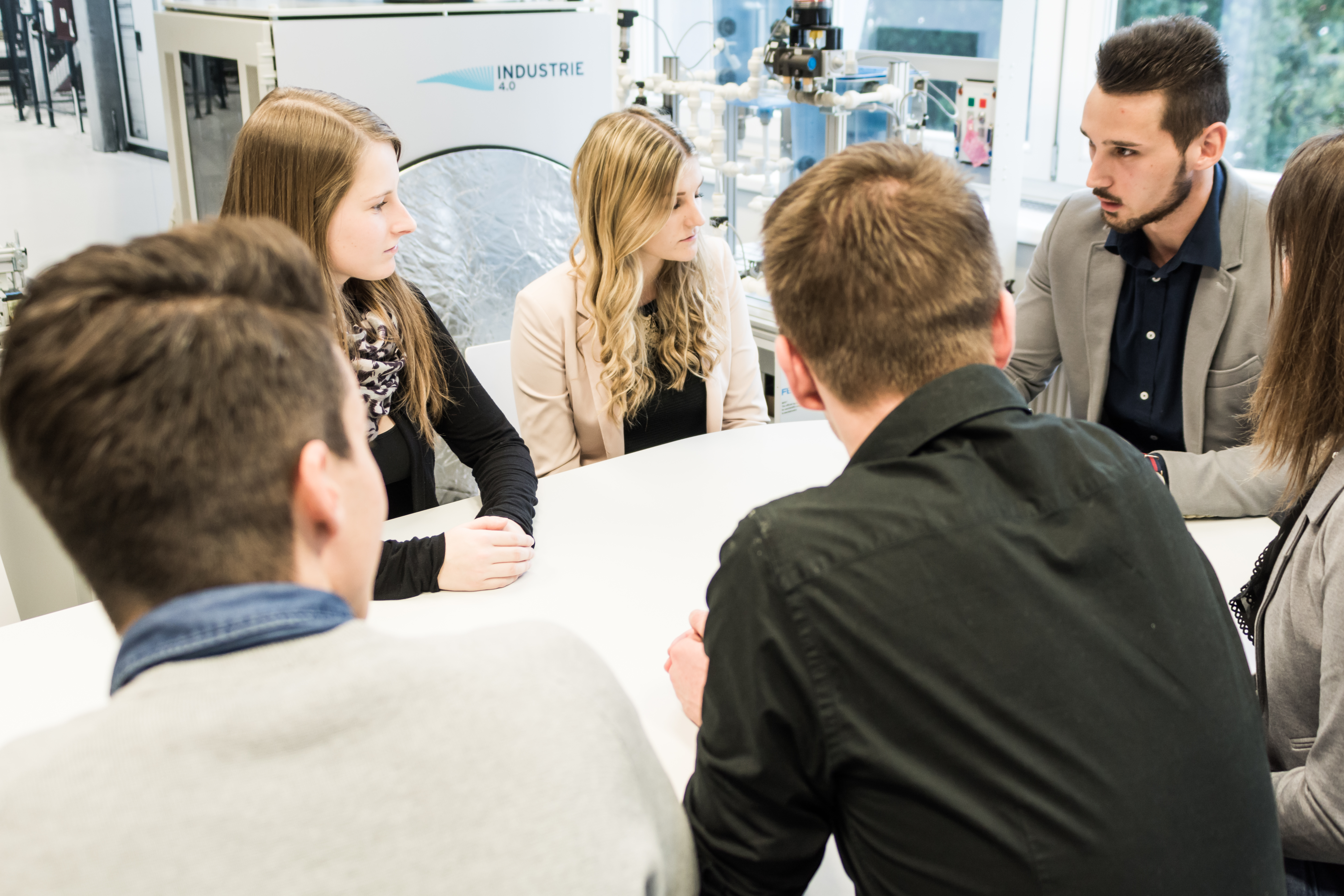 Studierende sitzen an einem Tisch und besprechen etwas.