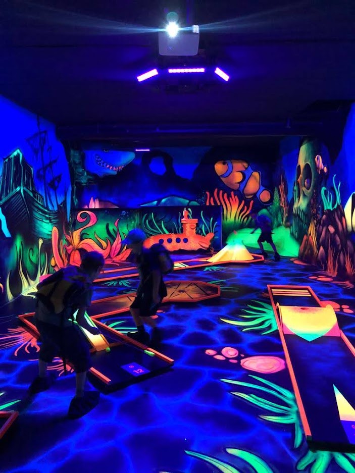 Kinder in einem dunklen Raum, der mit Neonlichtern beleuchtet ist.