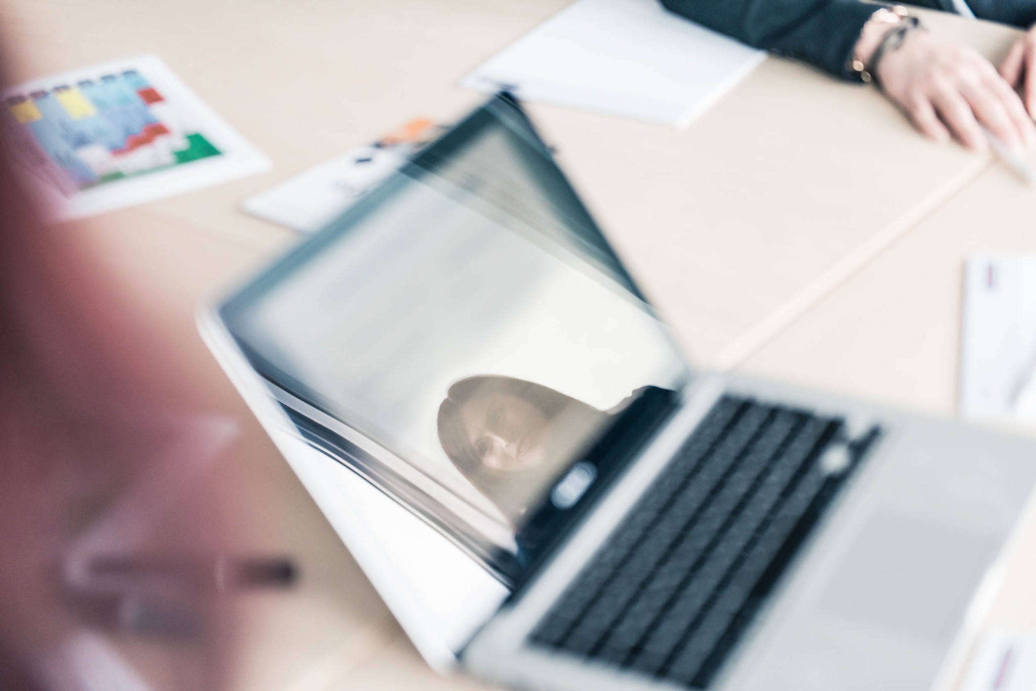 Laptop mit Spiegelung einer Frau am Tisch in einem Büro
