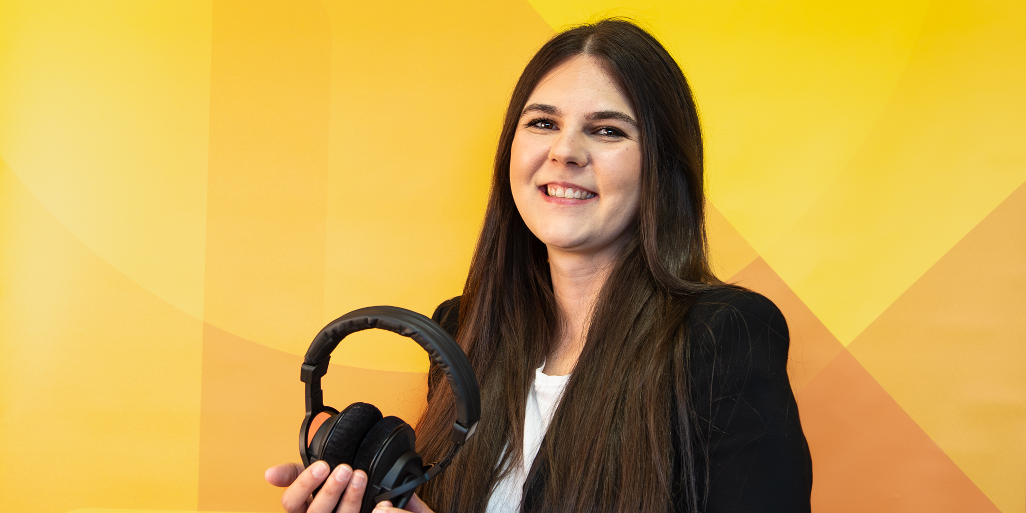 Matea Radoš steht mit Podcast-Kopfhörern vor einem gelben Hintergrund.