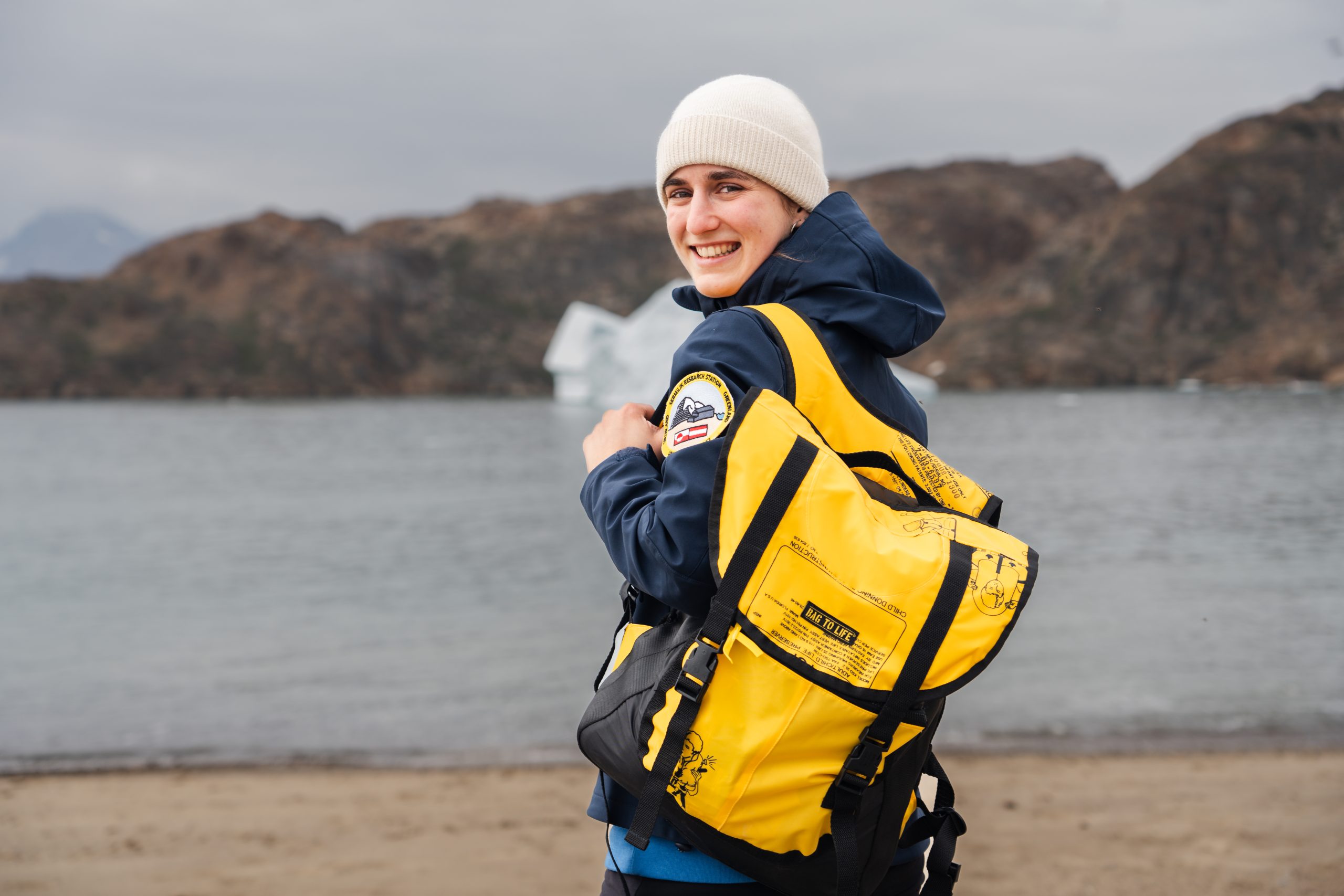 Junge Frau mit gelbem Rucksack vor dem arktischen Ozean