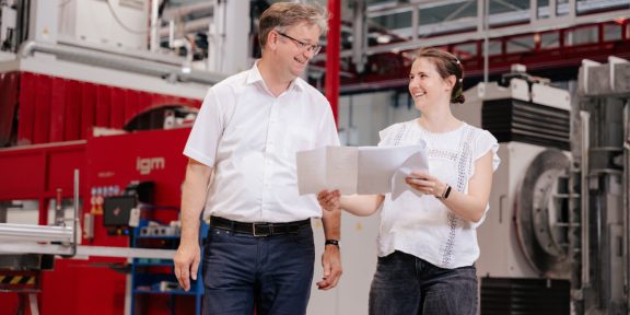 Mitarbeiter besprechen Pläne in einer Produktionshalle mit Maschinen