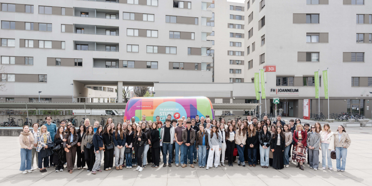 FH Joanneum Studierende vor dem Gebäude in Graz mit buntem Bus