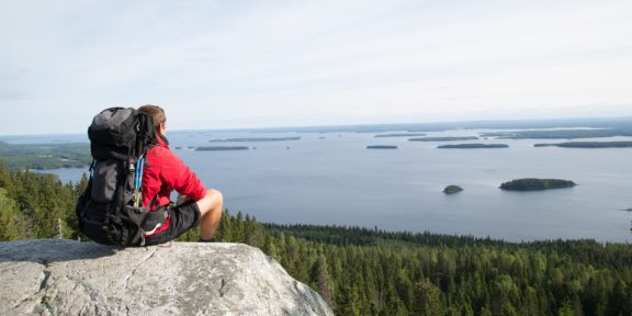 Wanderer mit Rucksack sitzt auf Felsen über See mit vielen Inseln